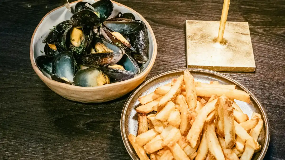 Moules-frites belgas: mejillones al vino blanco en cazuela negra con patatas fritas crujientes al lado